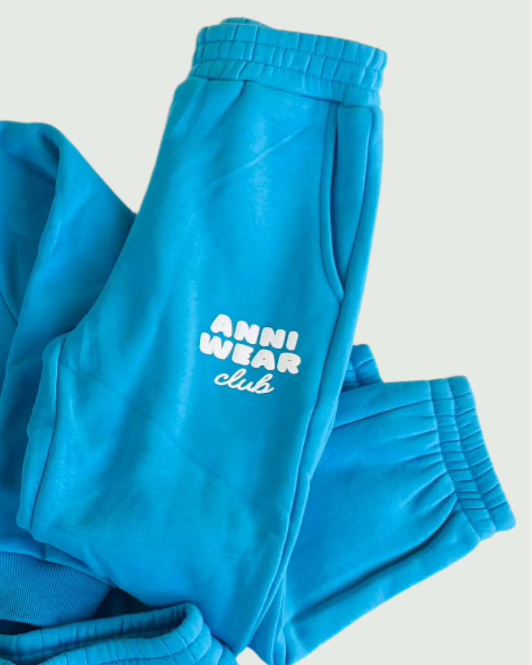 Blue tracksuit with 'Anni Wear Club' logo on a light gray background