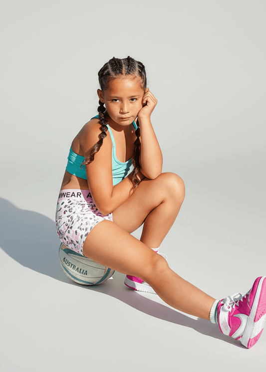 Young girl sitting on a ball wearing a sports outfit with a light gray background