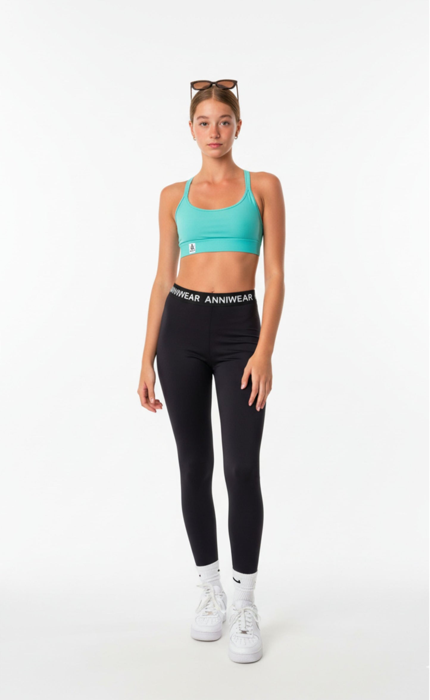 Teen Girl wearing a turquoise sports bra and black leggings with 'Anniwear' branding on a white background