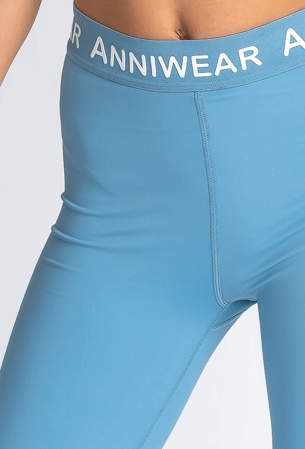 Blue leggings with 'ANNIWEAR' waistband on a light gray background
