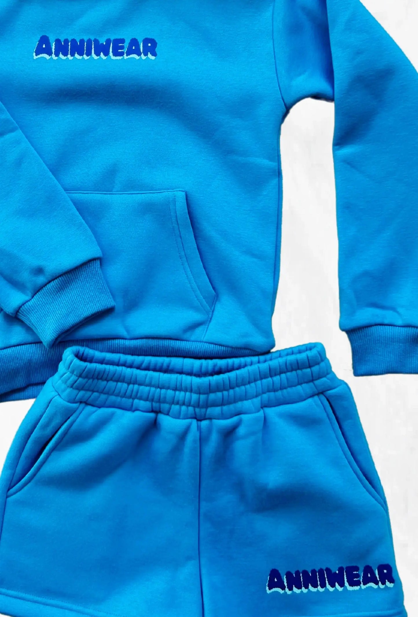 Blue sweatshirt and shorts set with 'Anniwear' logo branding on a light gray background