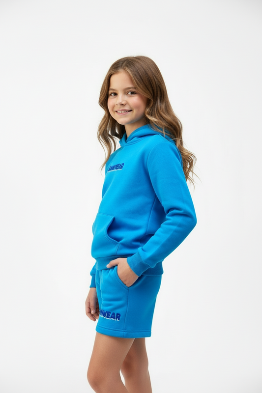 Young girl wearing a blue hoodie and shorts set on a white background