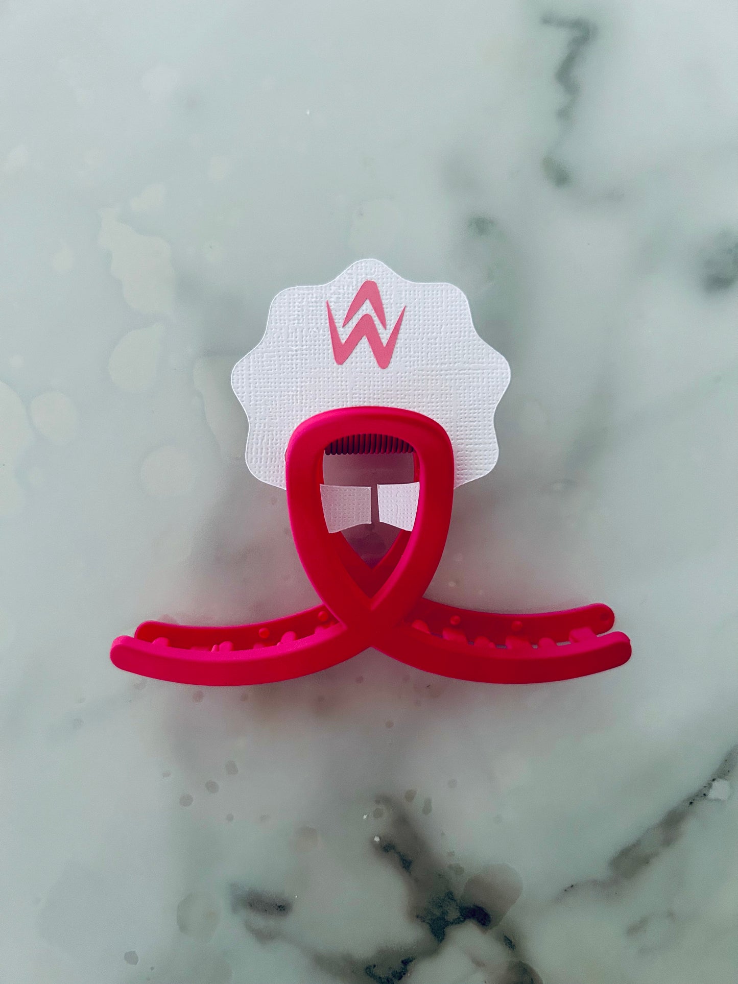 A pink hair claw clip placed on a white background with a decorative element above it.
