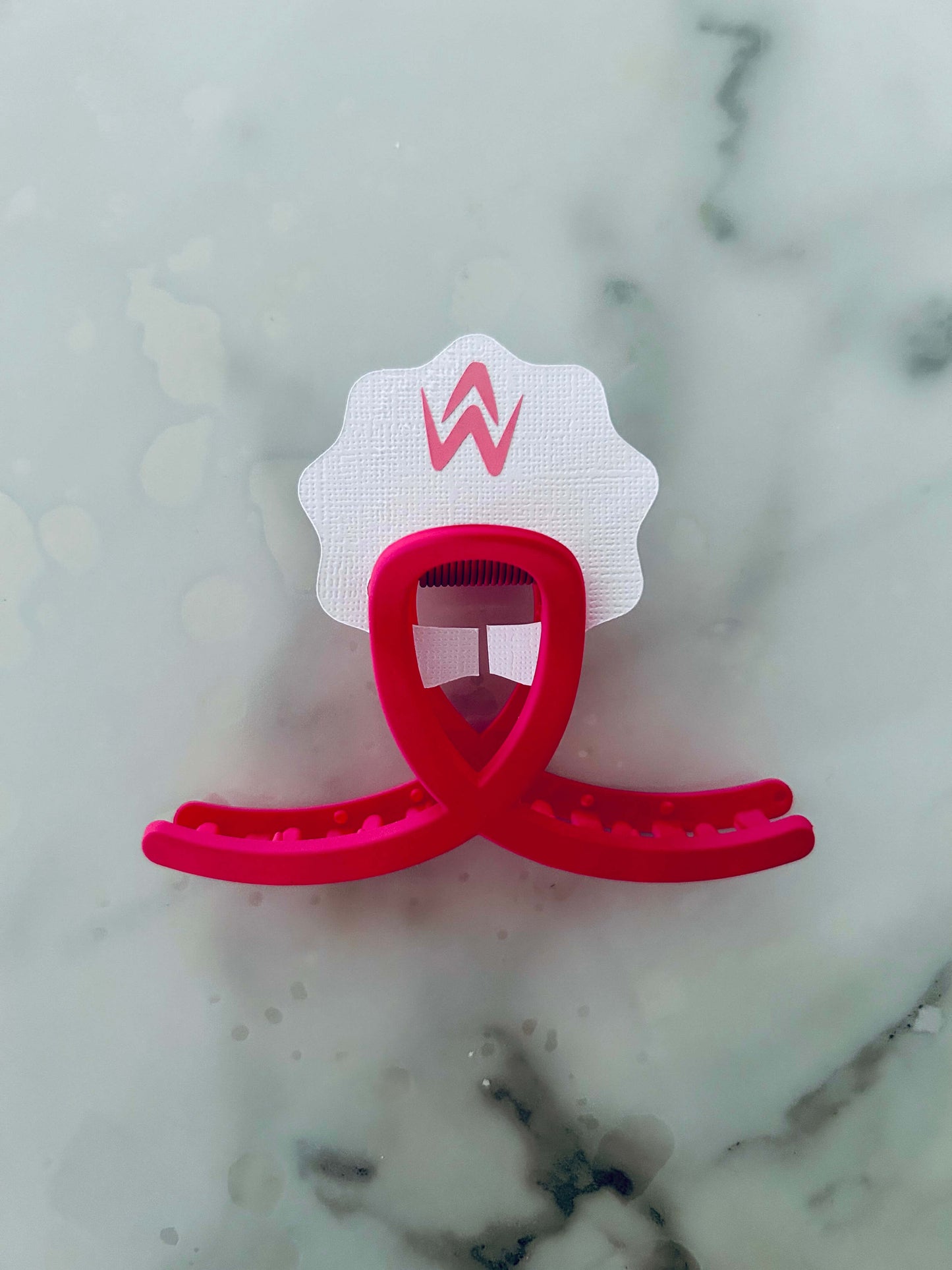 A pink hair claw clip placed on a white background with a decorative element above it.