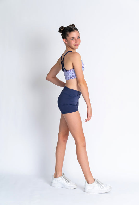 A female model wearing a lavender haze crop top and matching shorts, standing on tiptoe.