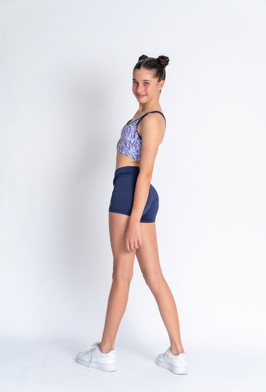A female model wearing a lavender haze crop top with a patterned design, paired with navy blue shorts,