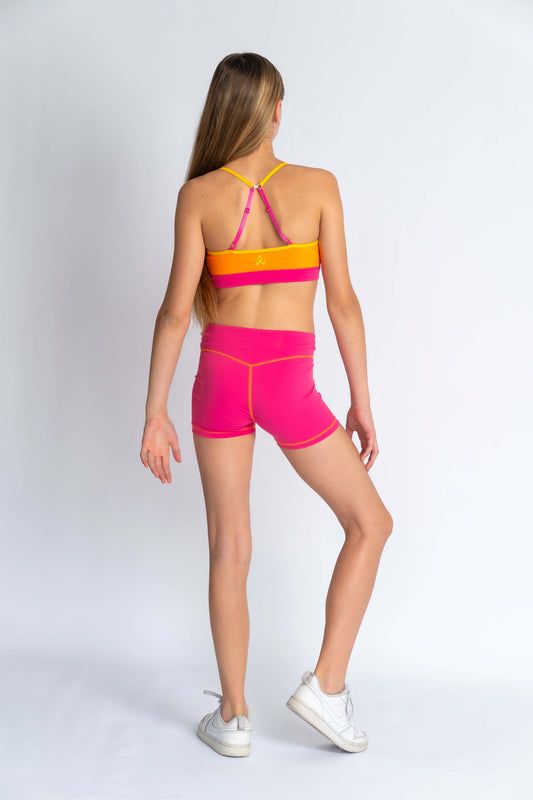 A back shot pose of a girl with an orange and pink crop top and pink shorts on a white background