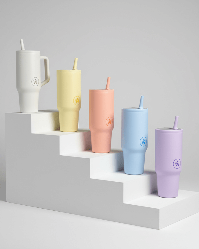 Set of colorful tumblers with straws on a geometric shelf against a gray background