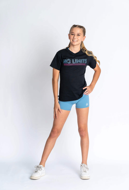 A young female model wearing a black No Limits Tee with a placement print on the chest and blue shorts, standing against a white background.