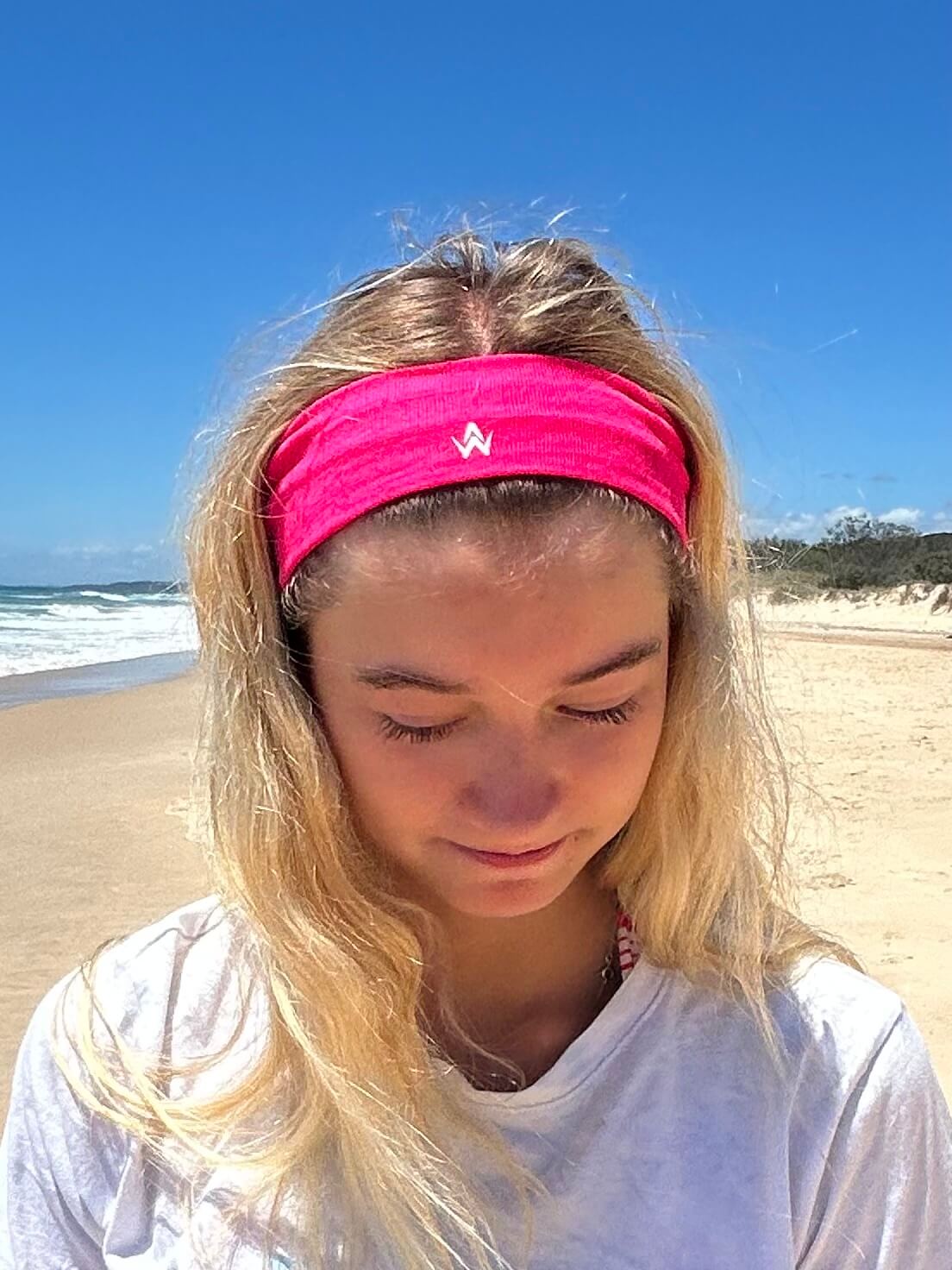 Person wearing a pink headband on a beach with blue sky and ocean in the background