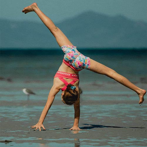 Young girl performing a handstand on a beach with mountains in the background