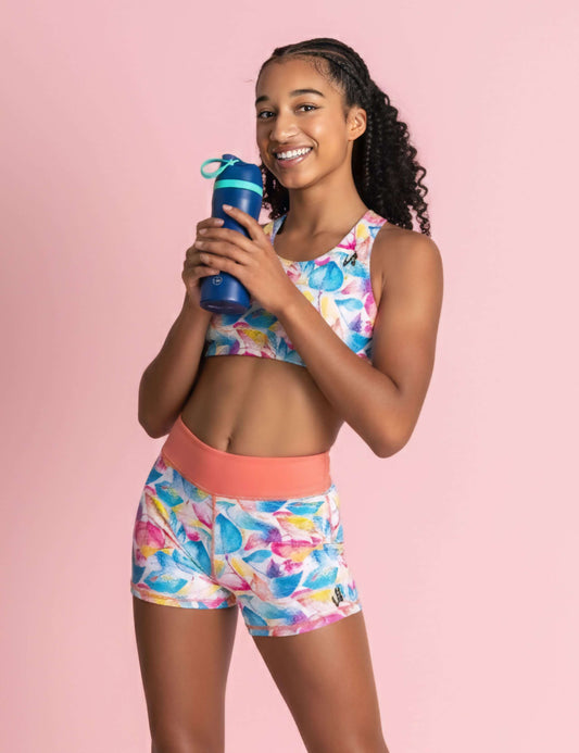 Young girl in colorful athletic outfit holding a water bottle against a pink background