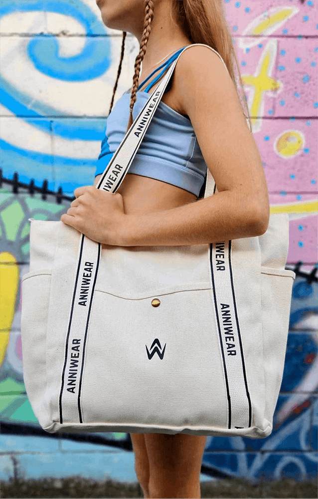 Beige canvas tote bag with black text and a logo worn on a girls shoulder wearing athletic sportswear