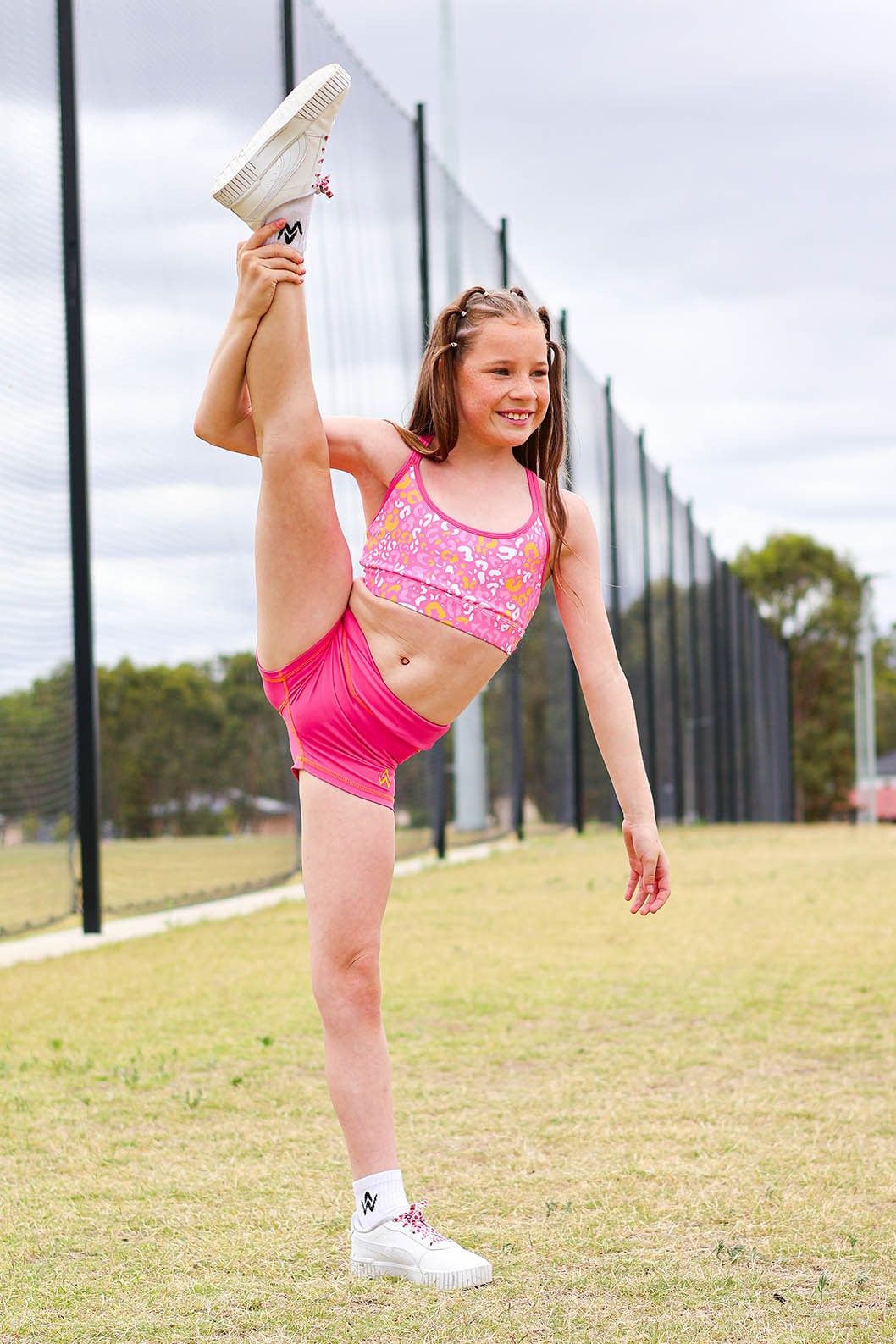 Young girl in a pink sportswear outfit stretching outdoors.
