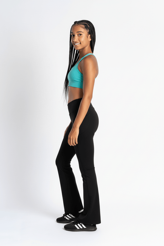 A girl modeling black flared athletic pants and a turquoise sports bra, standing in profile against a clean white studio background.