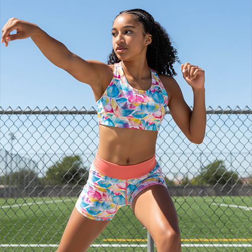 Girl in colourful athletic wear standing on a tennis court with a clear blue sky.