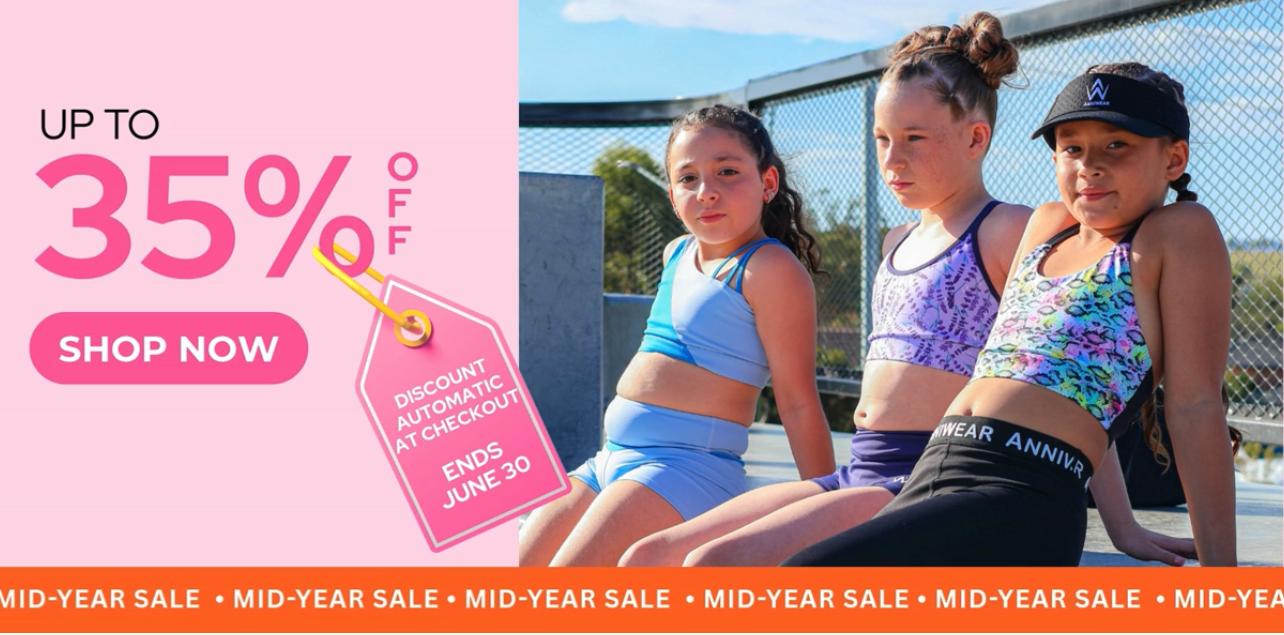 Three young girls in sports attire sitting on a tennis court with a promotional banner for a sale.