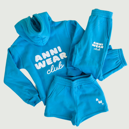 Blue tracksuit with 'Anni Wear Club' branding on a wooden surface