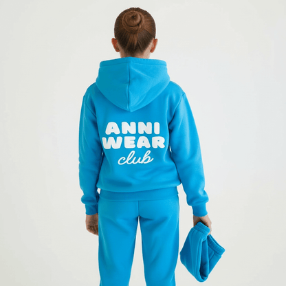 Person wearing a blue hoodie and pants with 'Anni Wear Club' text on the back, holding the shorts.
