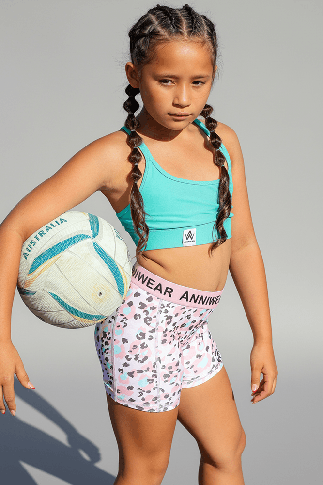 Young girl holding a soccer ball wearing a sports outfit with visible branding.