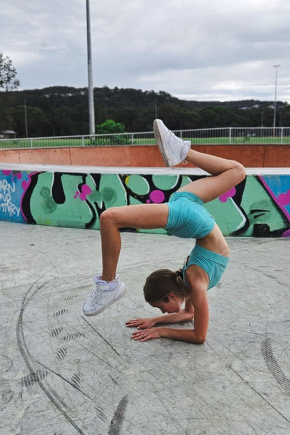 Person in turquoise outfit performing a yoga pose on a concrete surface with graffiti in the background.