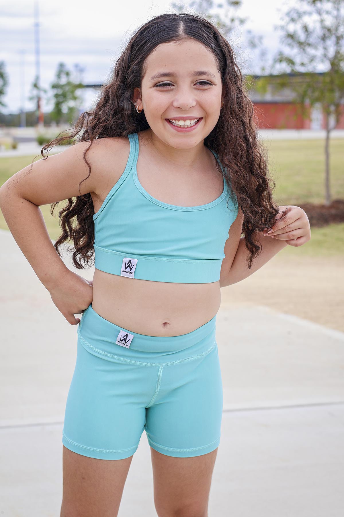 Young girl wearing a matching turquoise sports bra and shorts set outdoors.