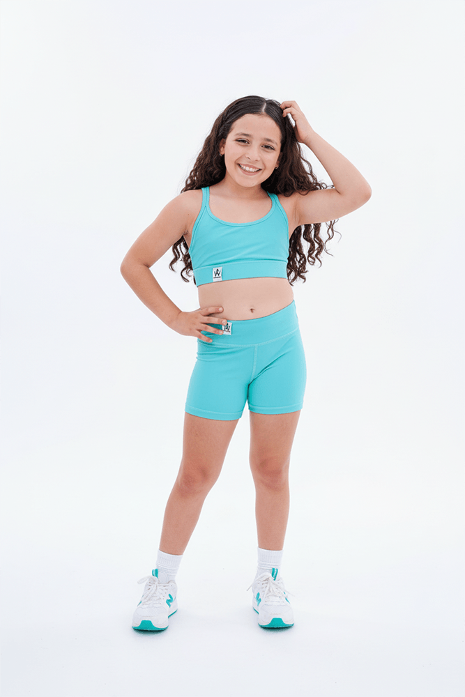 Young girl wearing a turquoise athletic outfit on a white background