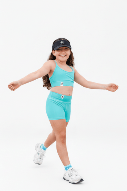 Child wearing a turquoise athletic outfit with a cap on a white background
