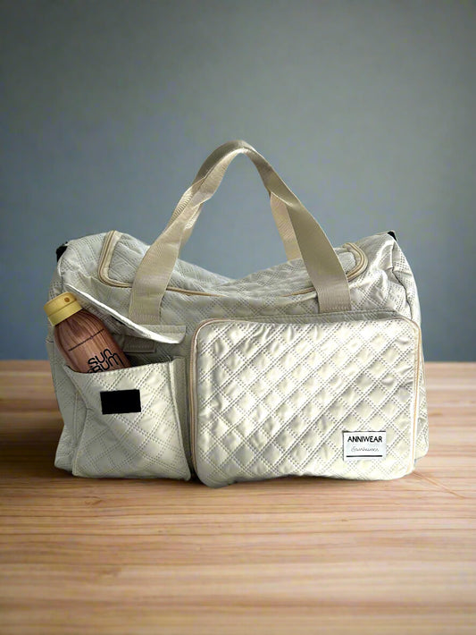 Sand coloured duffel bag with a bottle on a wooden surface and gray background