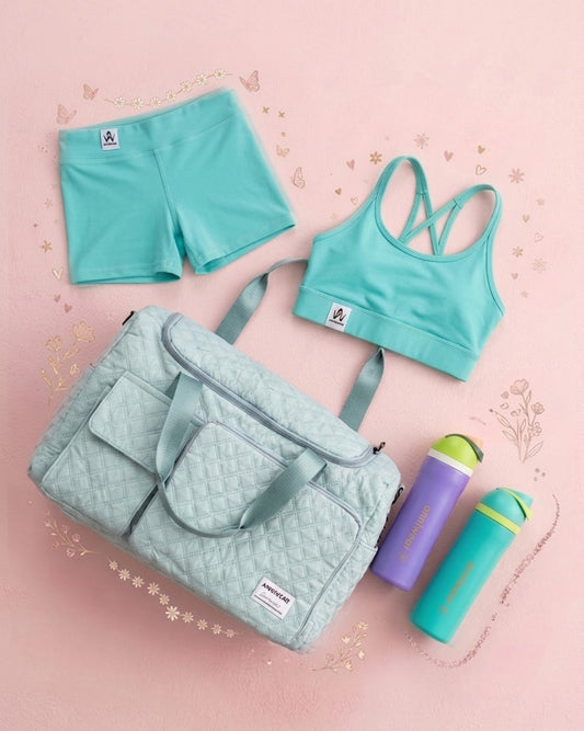 Teal sports bra and shorts set with a matching bag and water bottle on a pink background