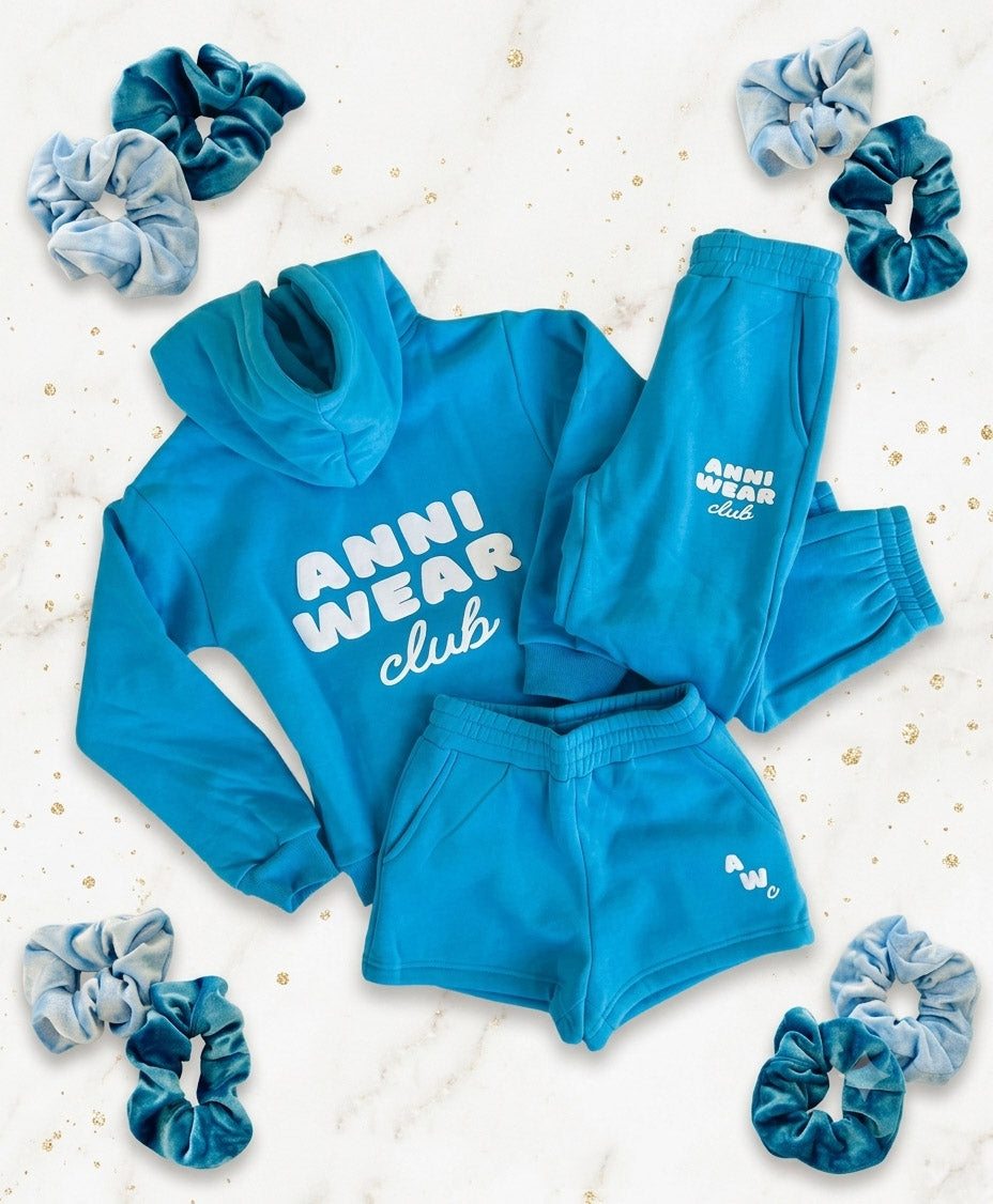 Blue athletic wear set with 'Anni Wear Club' text, surrounded by scrunchies on a light background