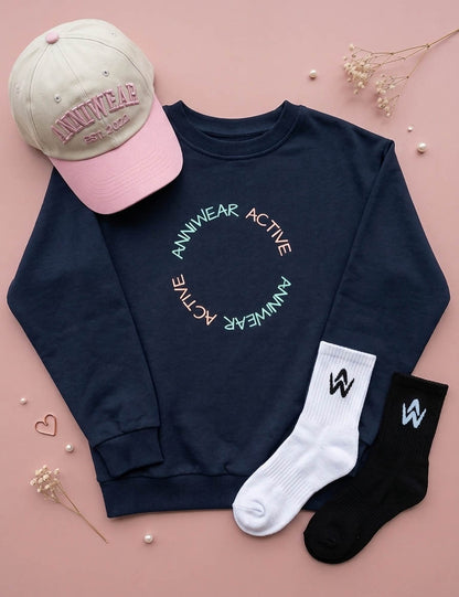 Navy sweatshirt with branding, pink cap, white socks, and black socks on a pink background