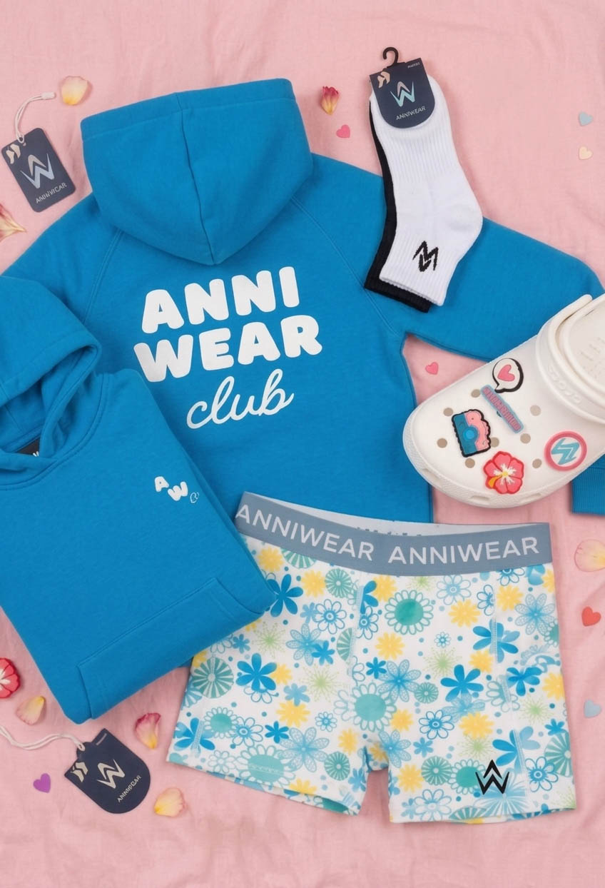 Blue hoodie with 'ANNI WEAR club' text, colorful shorts, socks, and a toy on a pink background.