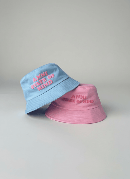 Two bucket hats, one blue and one pink, with 'Anni State of Mind' text on a light gray background.