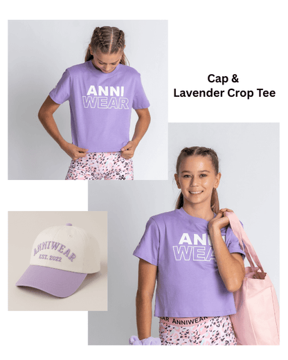 Two girls wearing lavender crop tees with 'ANNI WEAR' text, a matching cap, and pink tote bag.