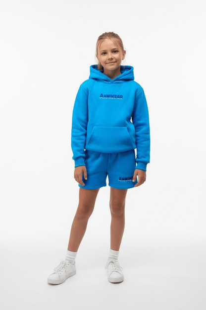 Child wearing a blue hoodie and shorts set with 'ANNIWEAR' branding on a white background