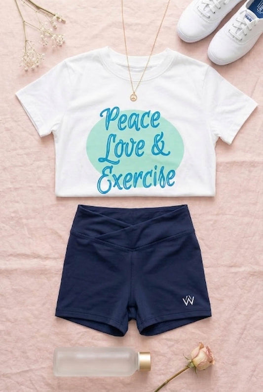 White t-shirt with 'Peace Love & Exercise' text, navy shorts, white sneakers, and a water bottle on a pink surface.