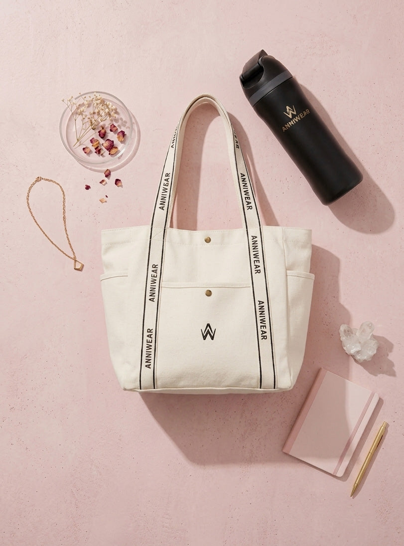 White tote bag with black text and a black water bottle on a pink background
