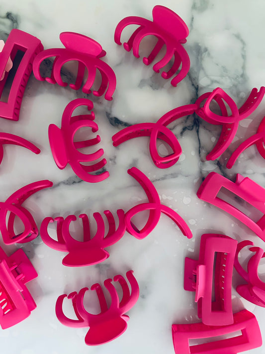 A collection of vibrant matte pink hair claw clips of various designs placed on a marble surface.