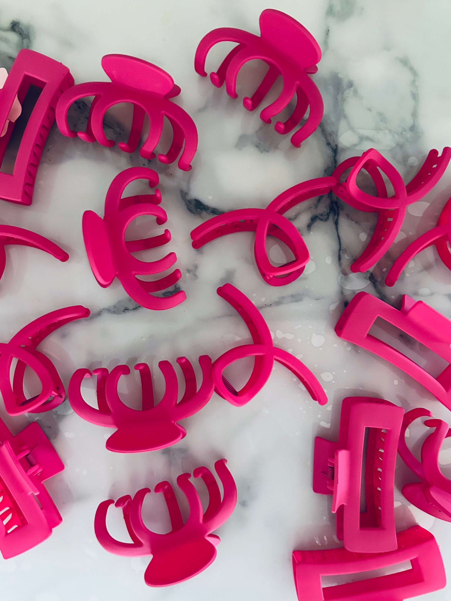 A collection of vibrant matte pink hair claw clips of various designs placed on a marble surface.