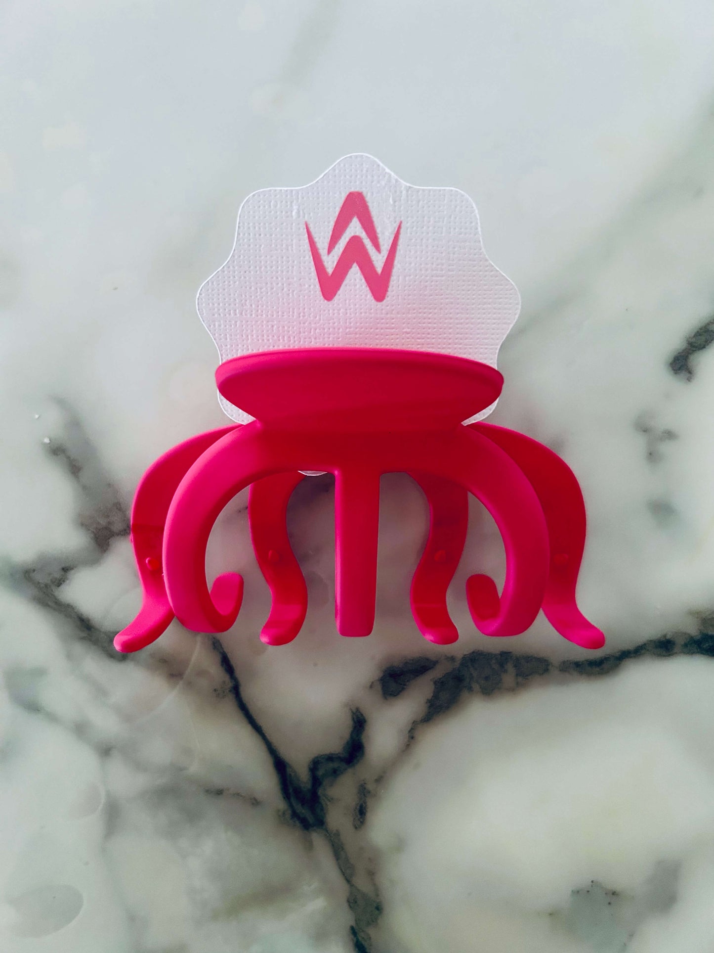 A pink hair claw clip placed on a white background with a decorative element above it.