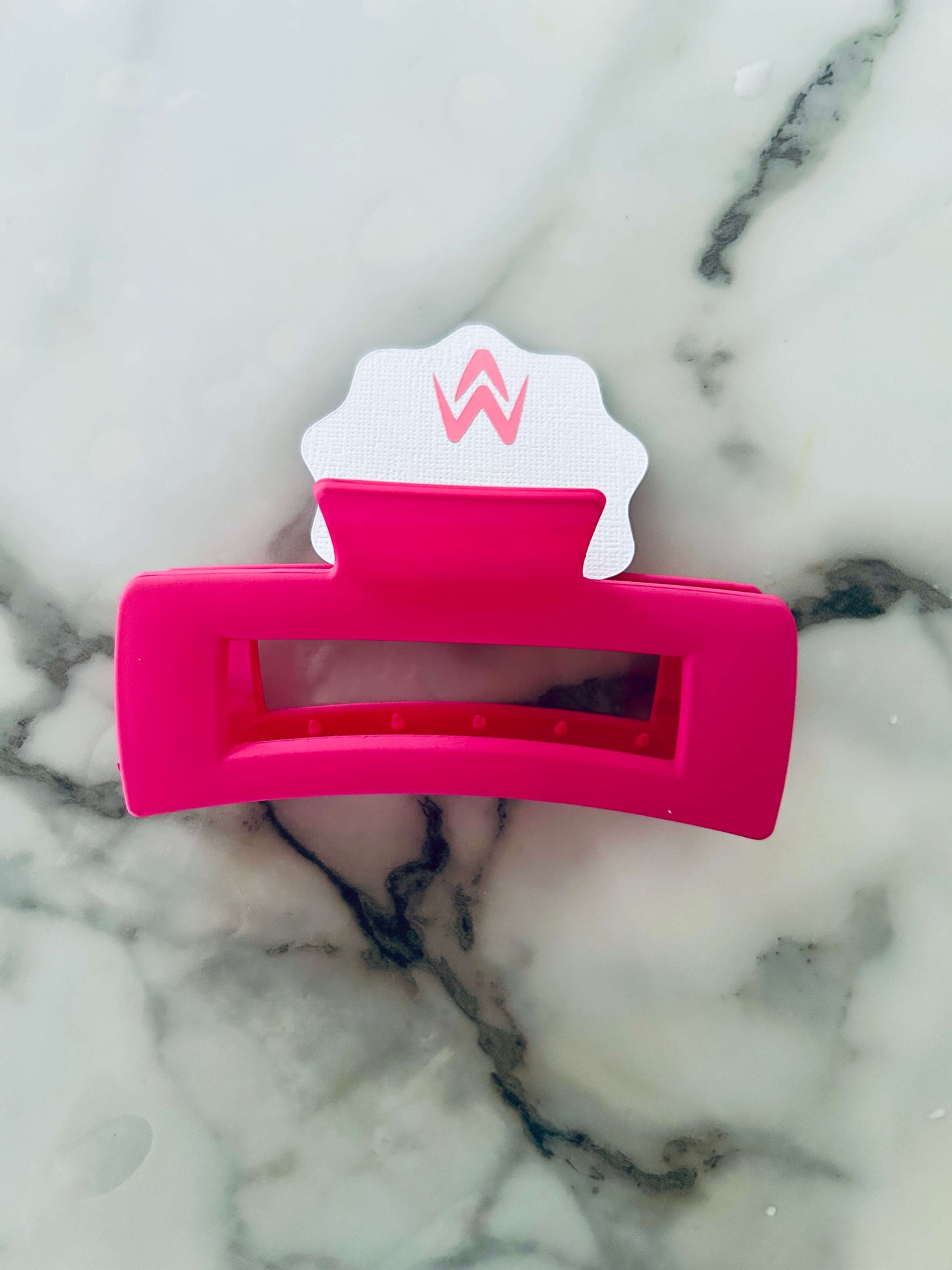 A pink hair claw clip placed on a white background with a decorative element above it.