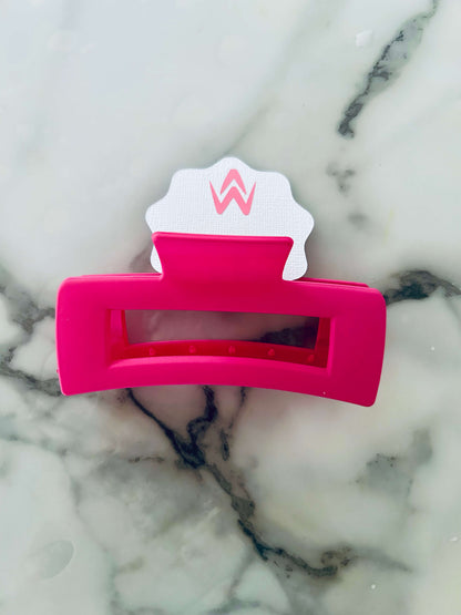 A pink hair claw clip placed on a white background with a decorative element above it.