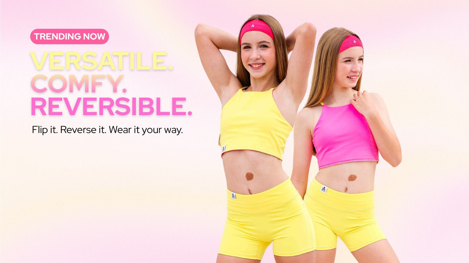 Two girls modeling reversible activewear sets in neon yellow and neon pink against a soft pink gradient background. The text on the left reads 'TRENDING NOW VERSATILE.