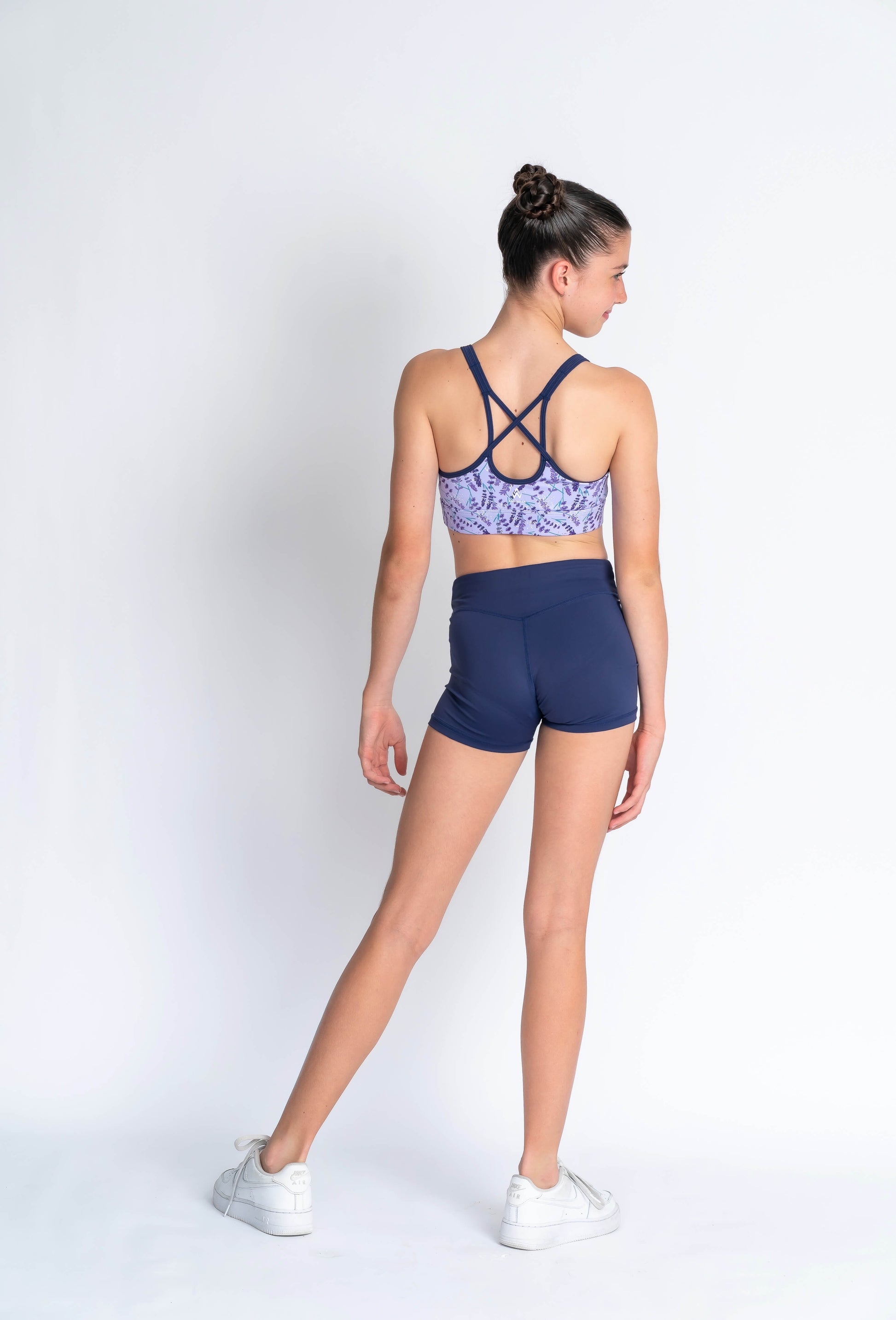 A female model wearing a lavender haze crop top with a patterned design, paired with navy blue shorts,