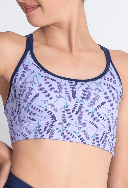 Woman wearing a purple sports bra with lavender print on a plain background