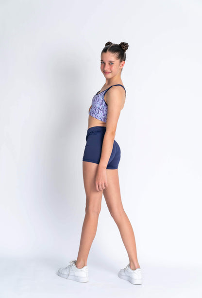A female model wearing a lavender haze crop top with a patterned design, paired with navy blue shorts,