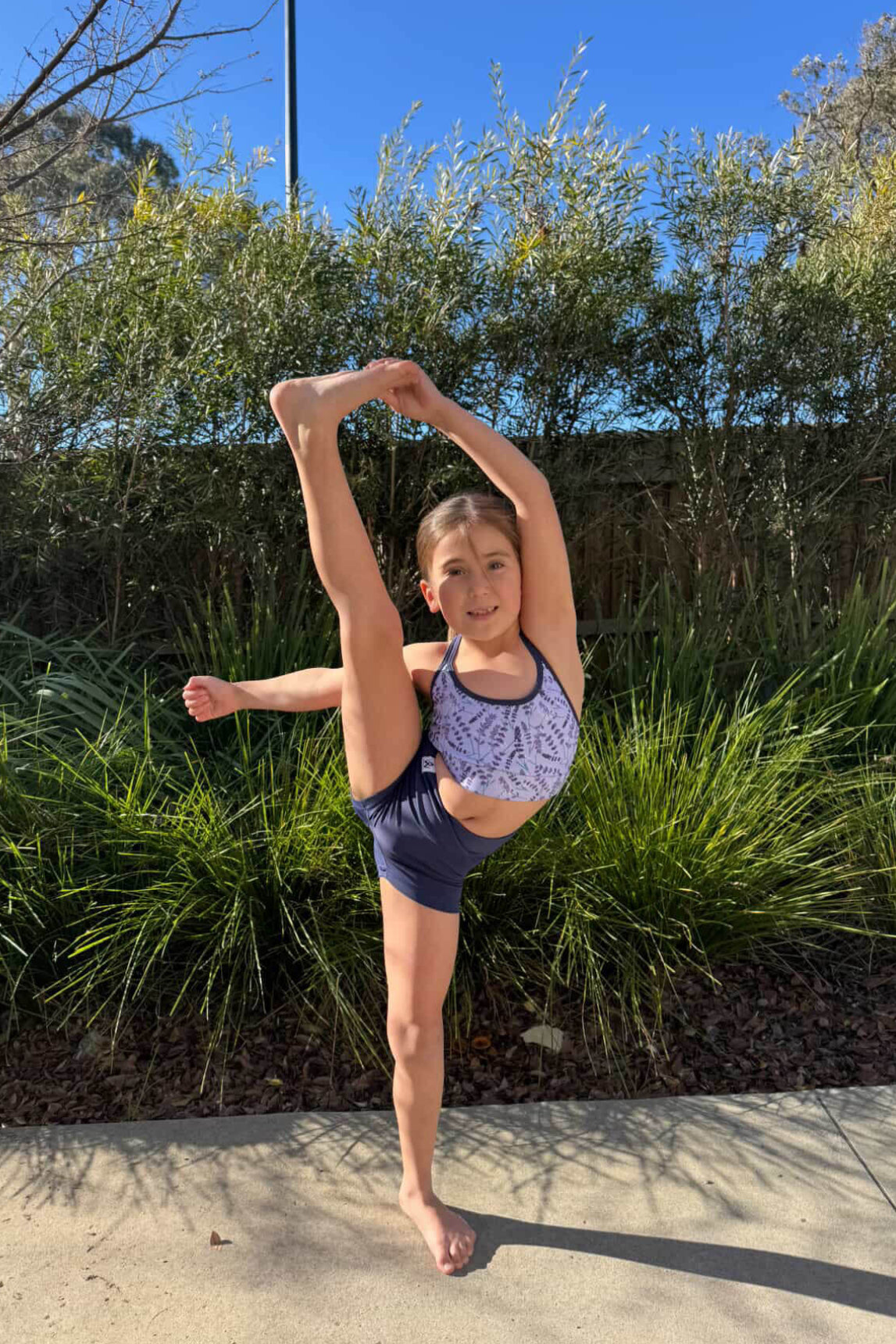 Young girl in a ballet pose outdoors with greenery in the background