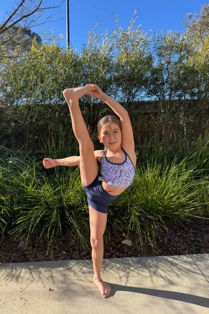 Young girl in a ballet pose outdoors with greenery in the background
