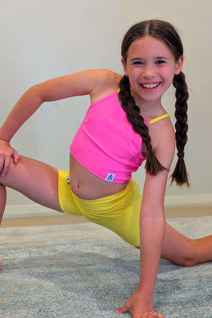 Young girl in pink top and yellow shorts posing on a carpeted floor.